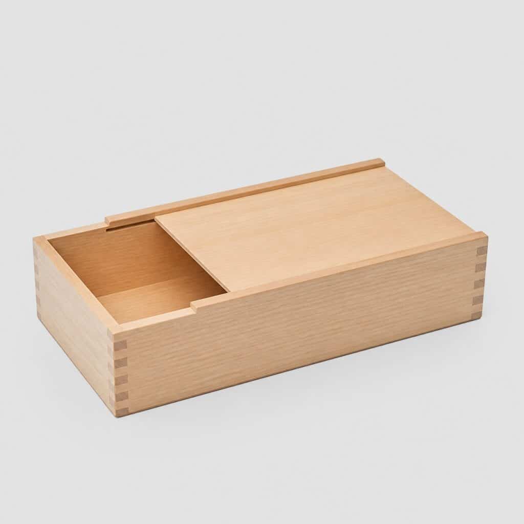 Boîte de rangement en bois clair à couvercle coulissant sur fond gris clair