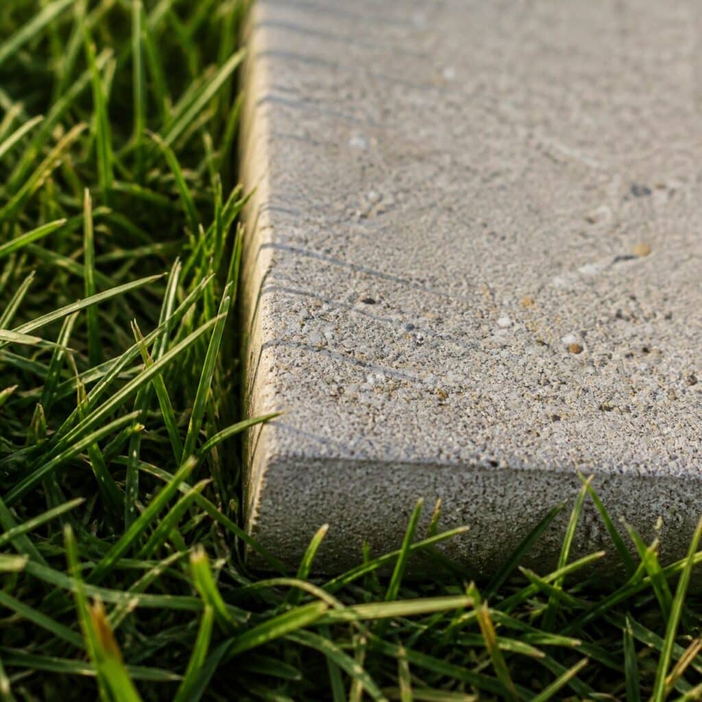Gros plan sur le bord de la dalle béton au contact des brins d'herbe