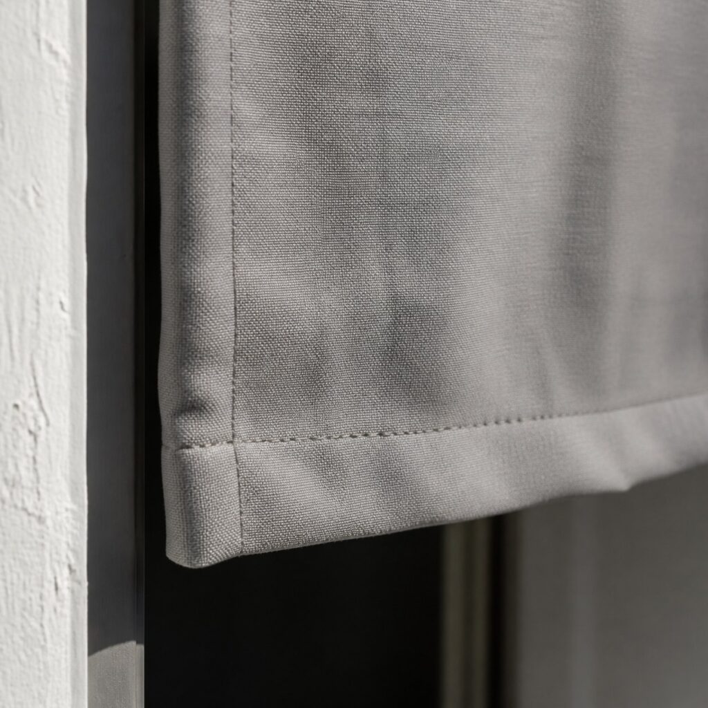 Gros plan sur l'ourlet inférieur et la couture latérale d'un rideau gris clair