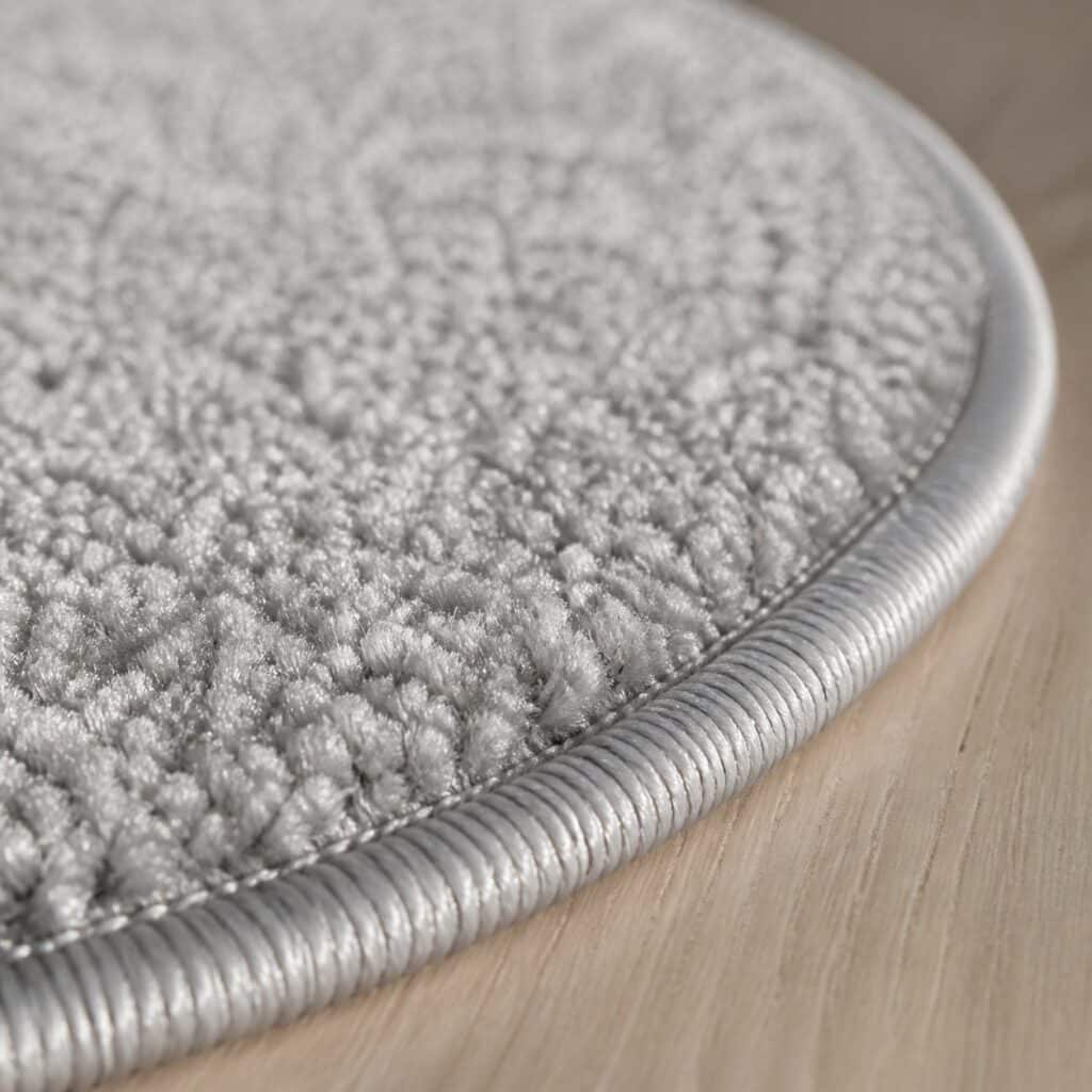 Gros plan sur la courbe et la finition bordée du pourtour d'un tapis rond gris
